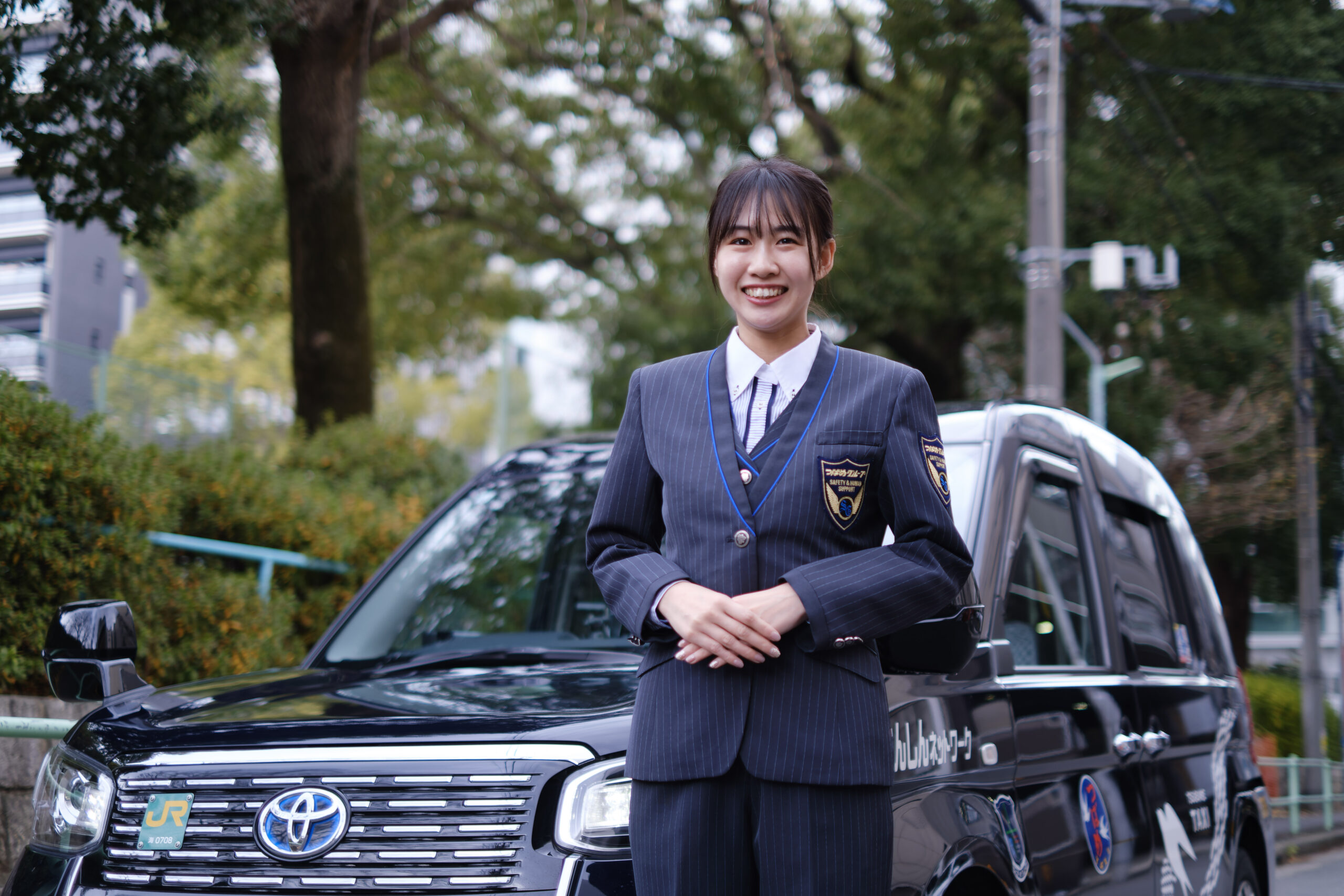 車の横に立ち、背筋を伸ばして笑顔のプロ意識の高い日本人女性ドライバー。