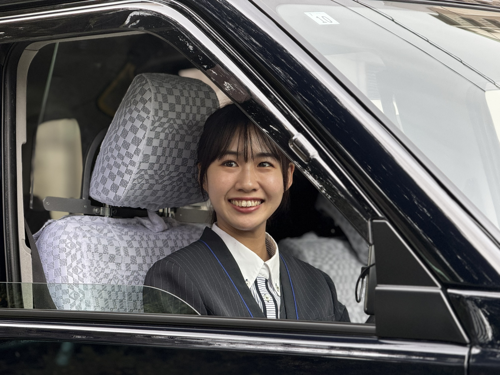 清潔感のある制服を着て、優しく微笑みながら前を見つめる日本人女性タクシードライバー。