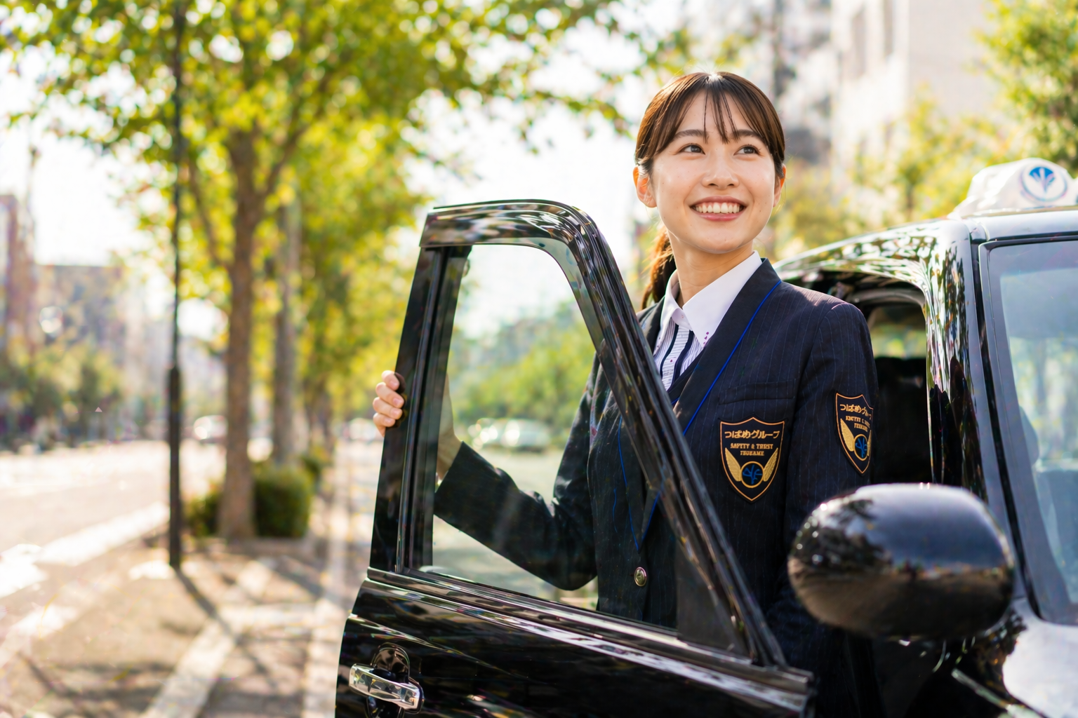つばめタクシーグループの制服を着た女性スタッフが黒色の車両ドアを開けて笑顔を見せ、収入アップや前向きなキャリア形成を表現した画像