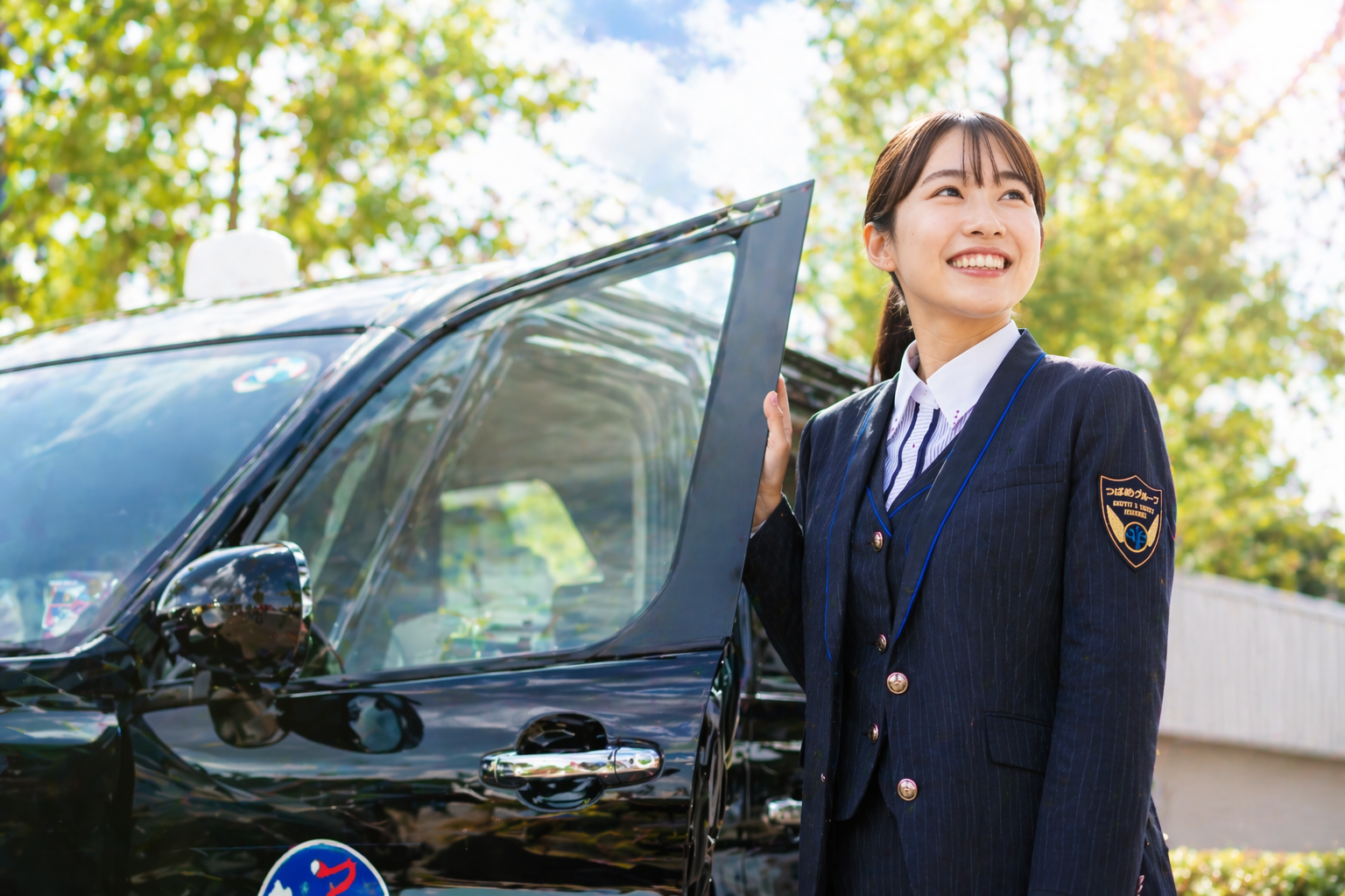 つばめタクシーグループの制服を着た女性が黒色の車両の前で考え込む表情を見せ、転職や未経験への不安を表現したイメージ画像