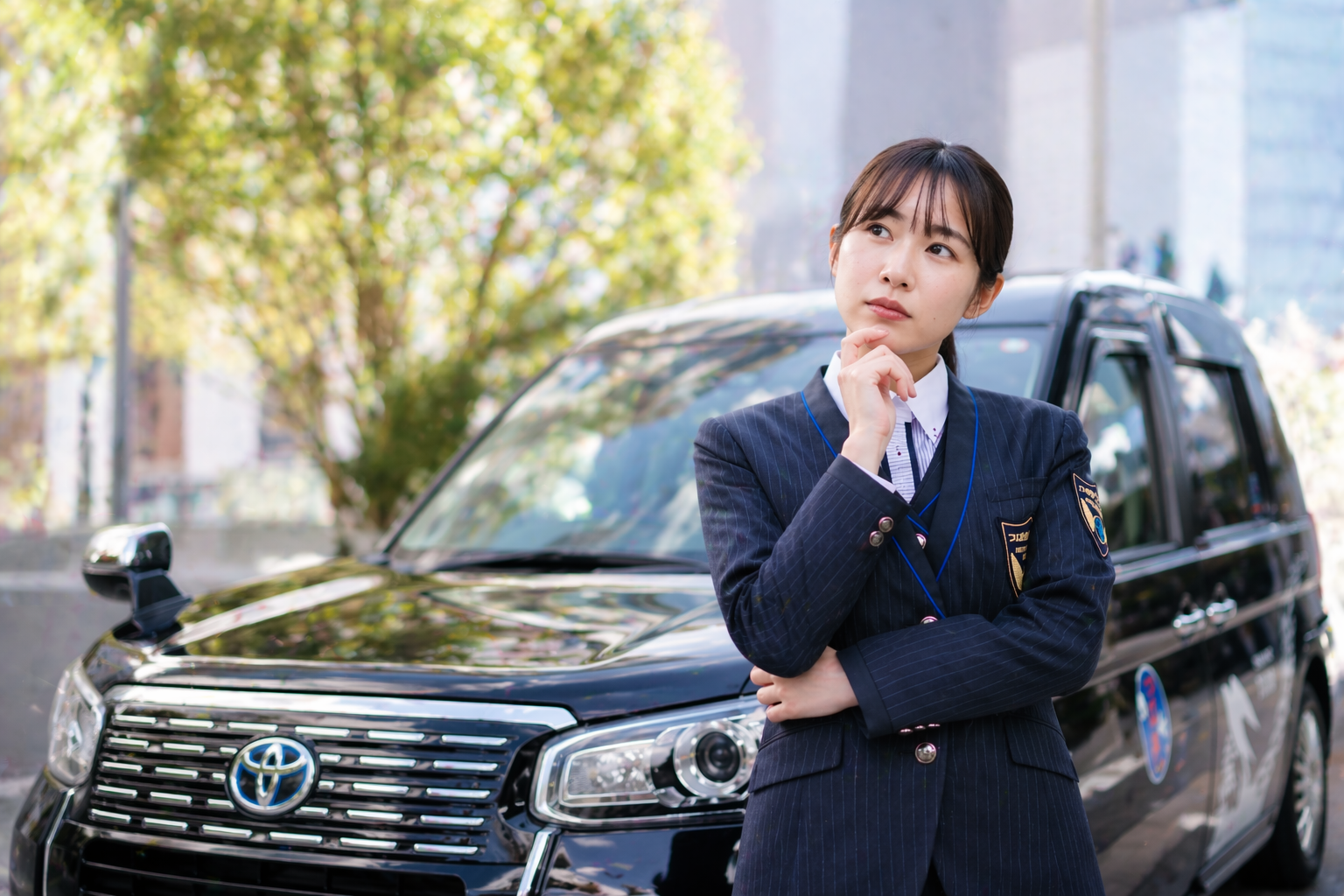 つばめタクシーグループの制服を着た女性が黒色の車両の前で考え込む表情を見せ、転職や未経験への不安を表現したイメージ画像